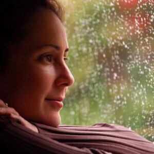 Woman looking out of rainy window with a slight smile on her face.