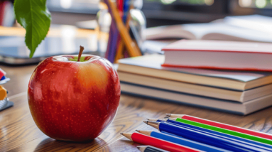 An apple and pens on a school desk.