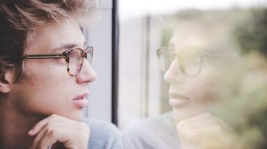 A man looking at his own reflection in the window of a train.