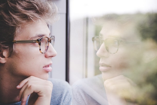 A man looking at his own reflection in the window of a train.