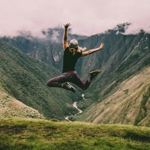 A woman jumping high in the green and lush mountains.