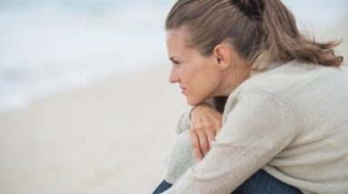 A sad woman sitting on a beach thinking.