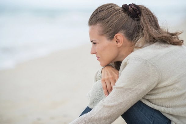 A sad woman sitting on a beach thinking.