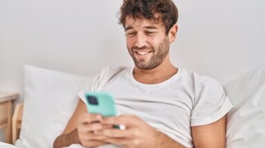 A happy guy sitting in bed reading on his phone.