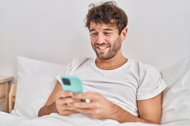 A happy guy sitting in bed reading on his phone.