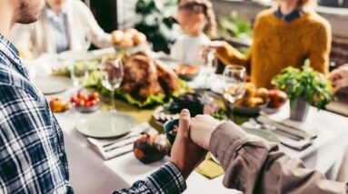 A family holding hands around a Thanksgiving dinner table.