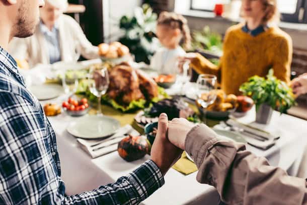 A family holding hands around a Thanksgiving dinner table.