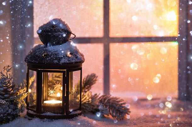 A Christmas lantern out in the snowy weather in front of a window.