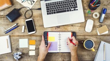 A person working with a computer and writing with a pen in a planner book.