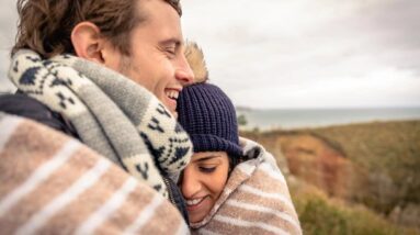 A couple hugging with blankets around them outside during fall.