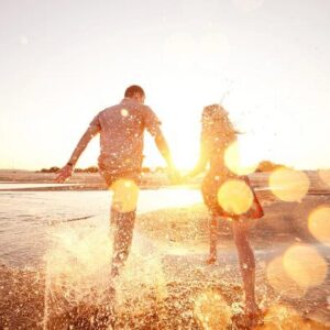 A happy couple running down the edge of the water on a beach during the golden hour.