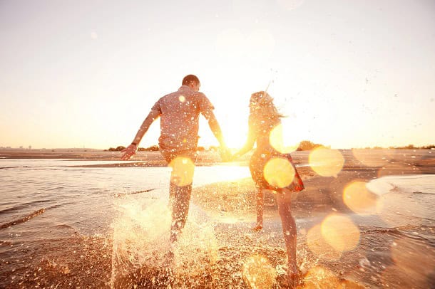 A happy couple running down the edge of the water on a beach during the golden hour.