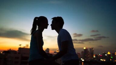 A couple about to kiss at sunset with a city in the background.