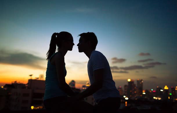 A couple about to kiss at sunset with a city in the background.