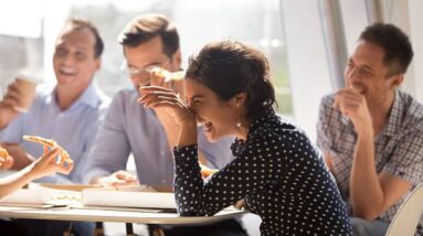 Coworkers laughing together while sitting around a table at work.