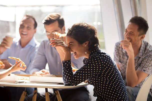 Coworkers laughing together while sitting around a table at work.