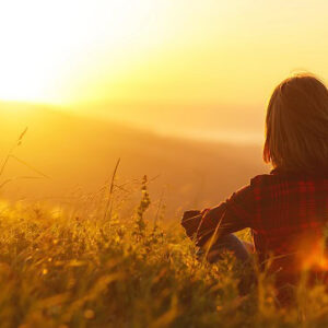 A woman sitting in a field and looking at a sunrise.