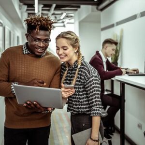 Co-workers in an office smiling while looking at a laptop screen.