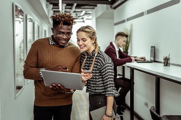 Co-workers in an office smiling while looking at a laptop screen.