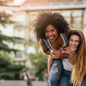 Two happy and confident women having fun in park, one of them riding on the other one's back.