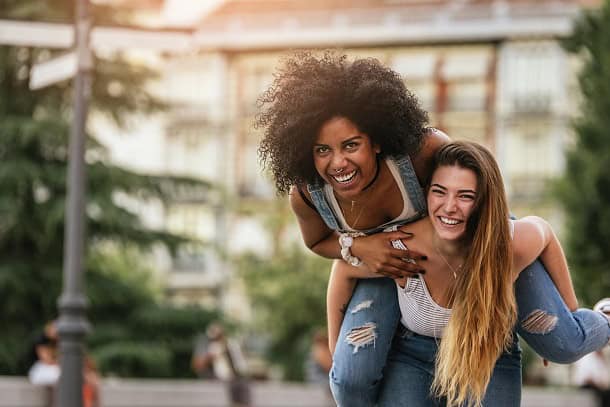 Two happy and confident women having fun in park, one of them riding on the other one's back.