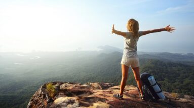 A happy woman with her arms stretched out at the top of a mountain.