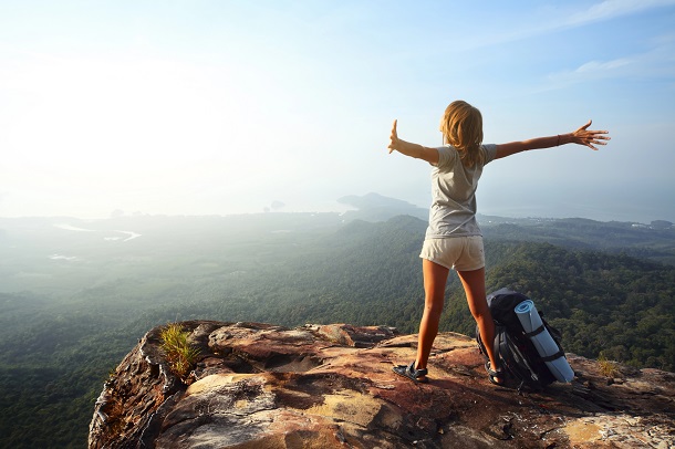 A happy woman with her arms stretched out at the top of a mountain.