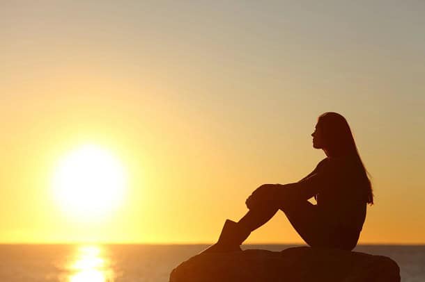 A woman looking at a sunset over the ocean.