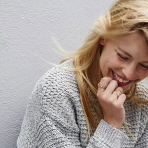 A smiling woman looking happy while standing against a white wall.