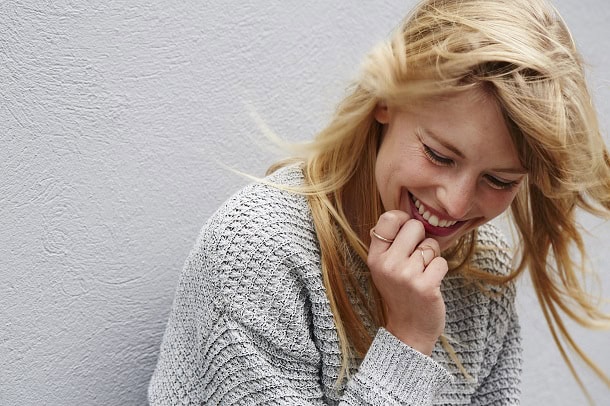 A smiling woman looking happy while standing against a white wall.