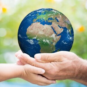 The Earth being held by one young hand and one old hand with a backdrop of green nature.