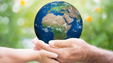 The Earth being held by one young hand and one old hand with a backdrop of green nature.