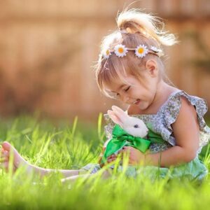 A happy little girl sitting the spring grass with a small white bunny.