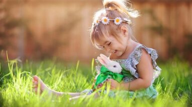 A happy little girl sitting the spring grass with a small white bunny.