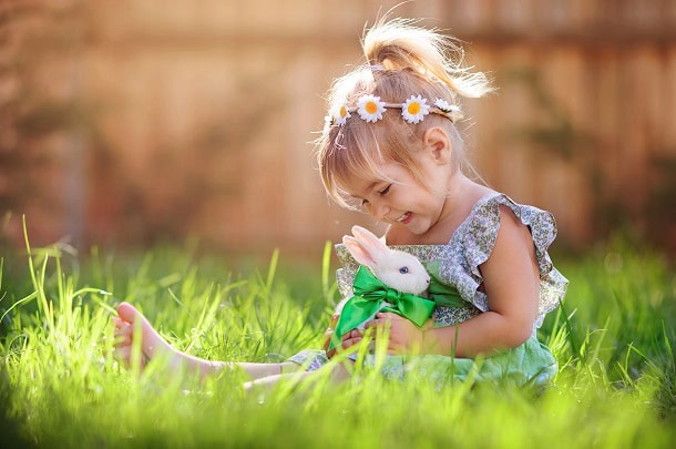 A happy little girl sitting the spring grass with a small white bunny.