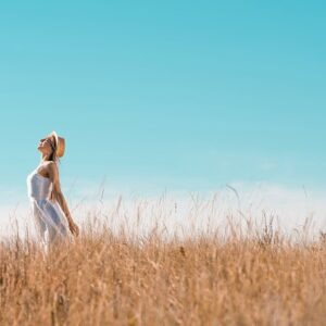 A woman stretching towards a blue sky while standing in a field.