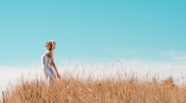 A woman stretching towards a blue sky while standing in a field.