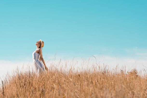 A woman stretching towards a blue sky while standing in a field.