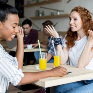 Two girls having a good time in a cafe with juice glasses.