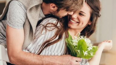 A happy man and woman hugging as the man gives the woman a bouquet of flowers.