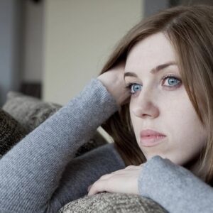 A woman looking sad while sitting on a couch.