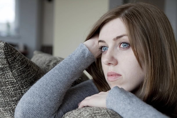 A woman looking sad while sitting on a couch.