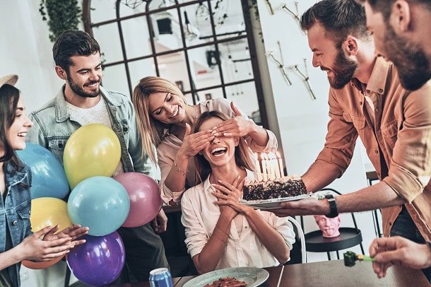Friends surprising the birthday girl with a cake with candles.