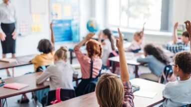 Kids sitting in class with their hand up.