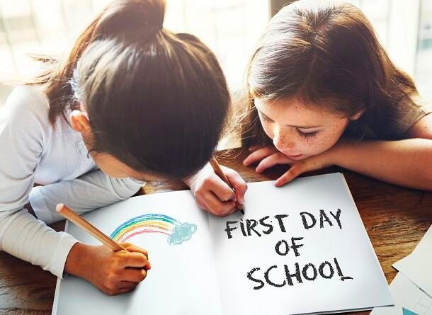 Two girls in school coloring a rainbow and writing: First Day of School.