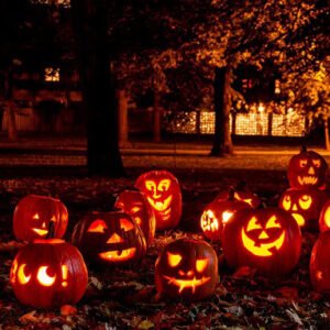 A group of carved pumpkins in a park at night with spooky darkness and yellow light.