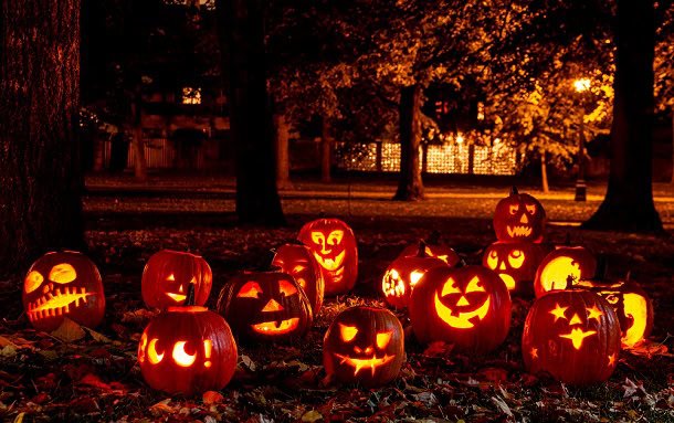 A group of carved pumpkins in a park at night with spooky darkness and yellow light.