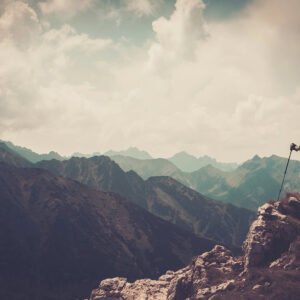 A woman who has climbed a mountain peak looking out at the impressive view.