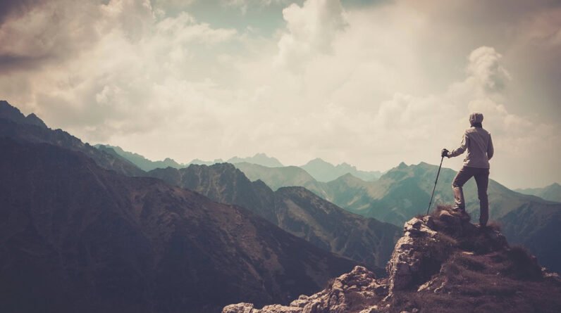 A woman who has climbed a mountain peak looking out at the impressive view.