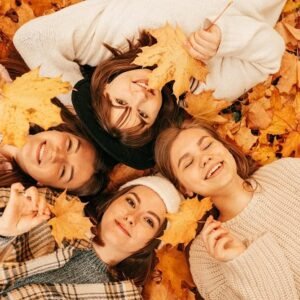Smiling women lying on the ground in fall leaves.